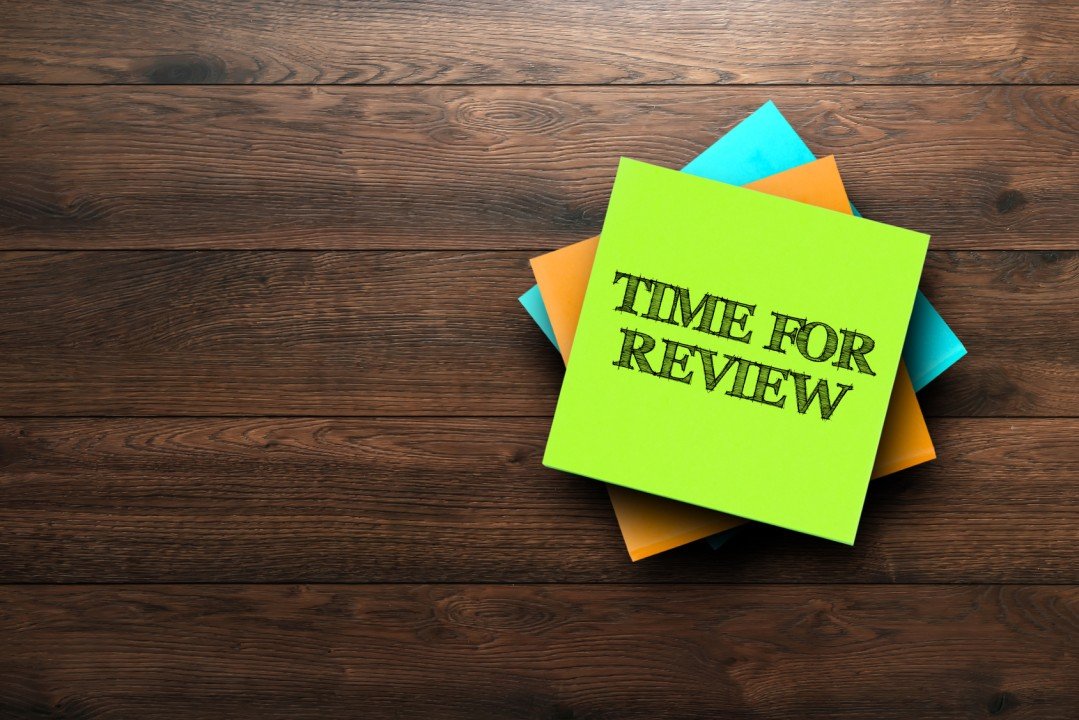 A stack of colorful sticky notes on a wooden background with "Time for Review" written on top, highlighting the importance of evaluating employee benefits.